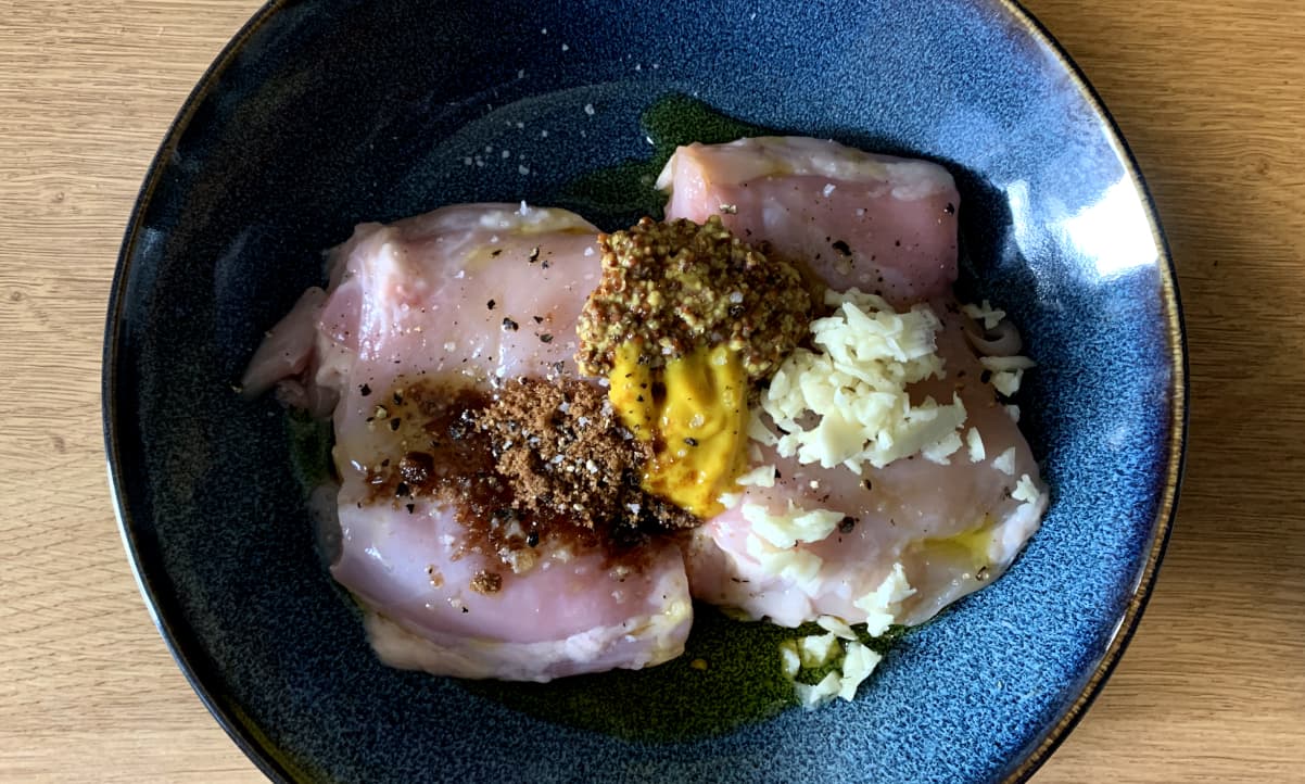 uncooked chicken thighs with various spices on top, including yellow mustard, wholegrain mustard, minced garlic and brown sugar