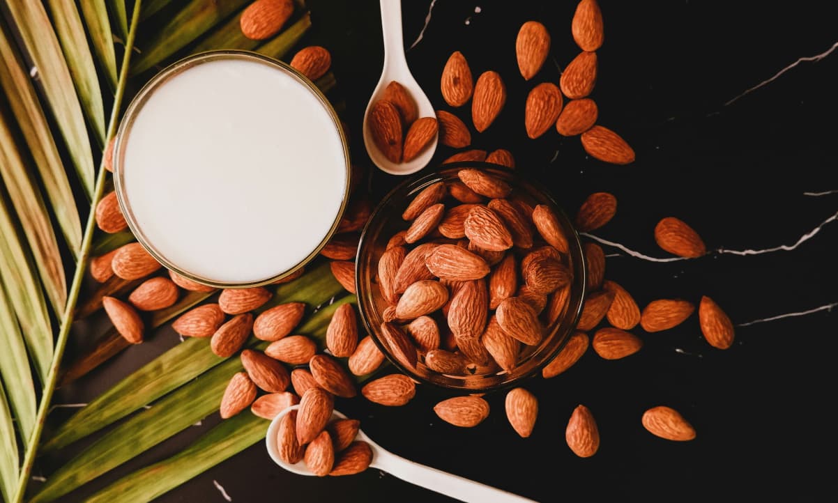 almonds scattered on a dark table next to a glass of almond milk