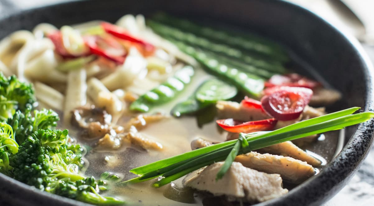 a closeup of ramen broth, garnished with fresh green vegetables and red chillis