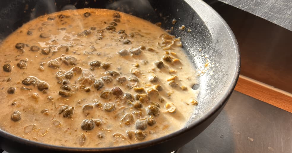 a closeup of creamy caper sauce in a black saucepan