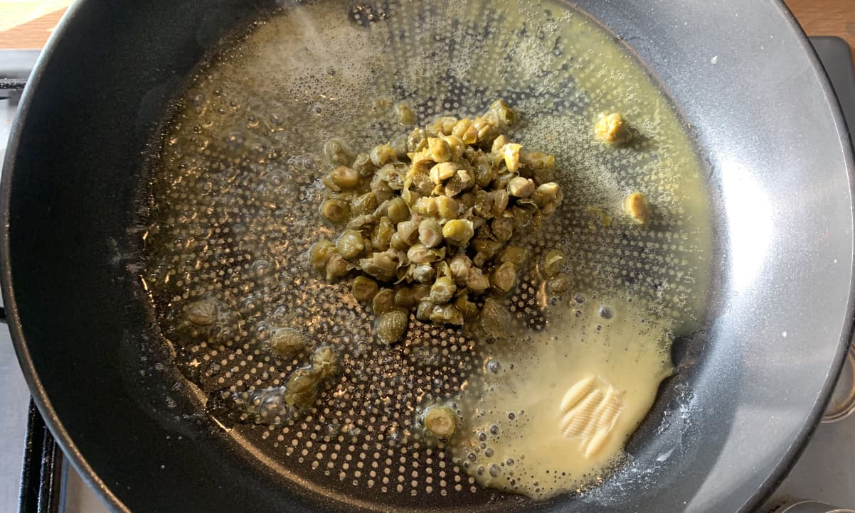 a pile of capers frying in melted butter in a black pan