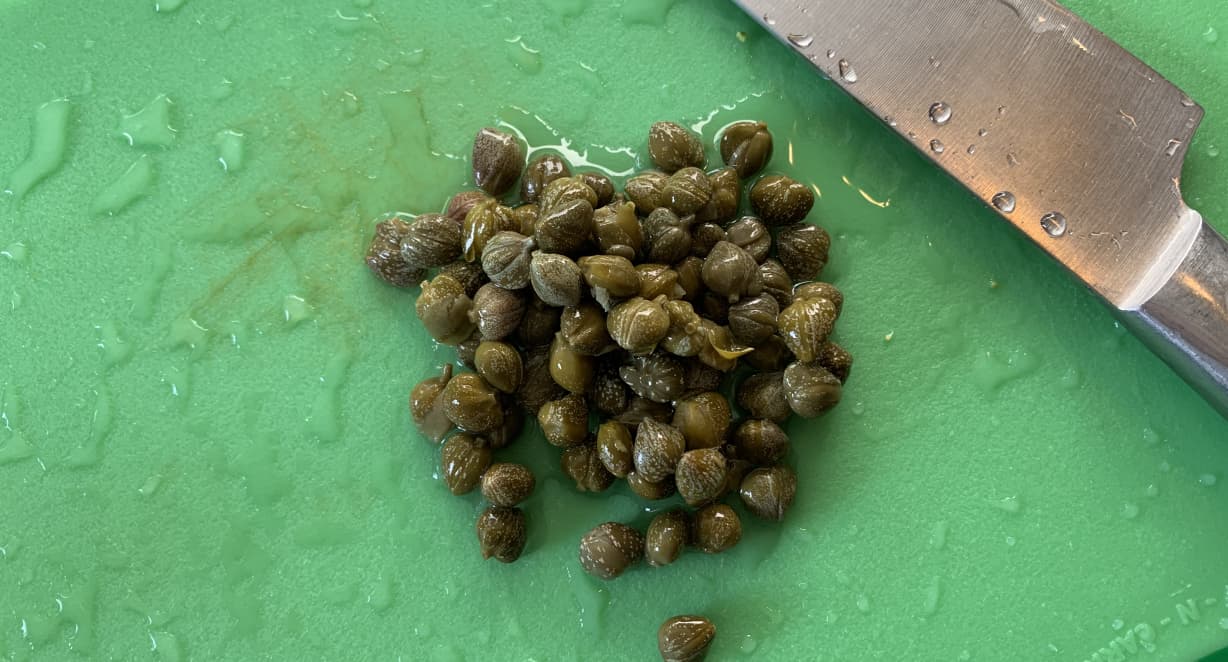 a small pile of capers on a green chopping board