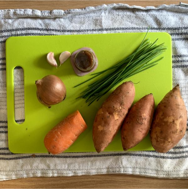 a selection of soup ingredients, including carrot, sweet potatoes, chives, onion, and two garlic cloves