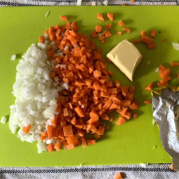 diced carrot and onion on a chopping board next to a knob of butter