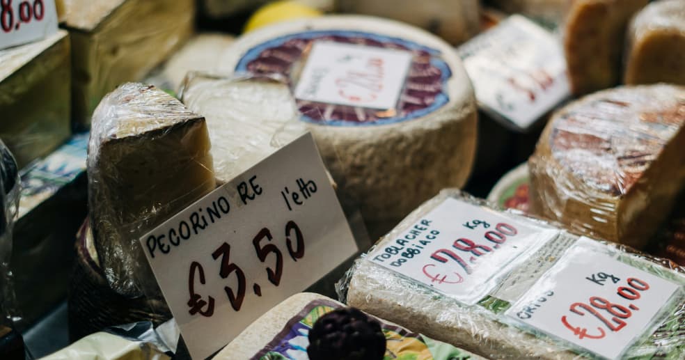 a selection of wheels of cheeses in a deli with price tags in Italian