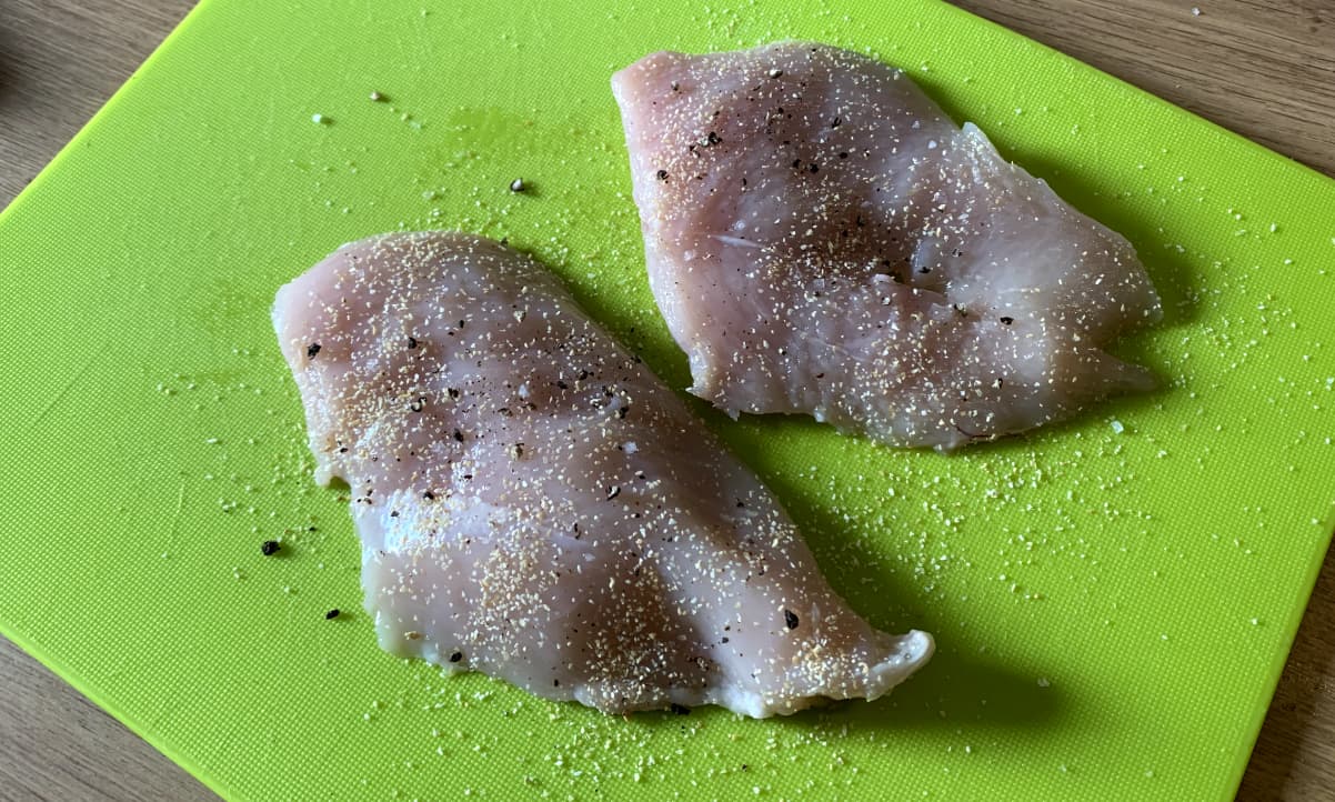 chicken breast seasoned with garlic granules, salt and pepper on a green chopping board