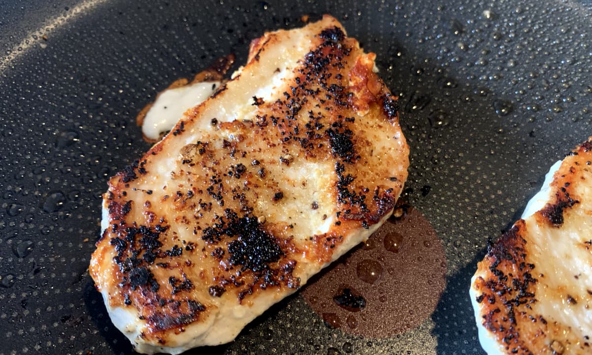 chicken with blackened garlic granules frying in a black pan