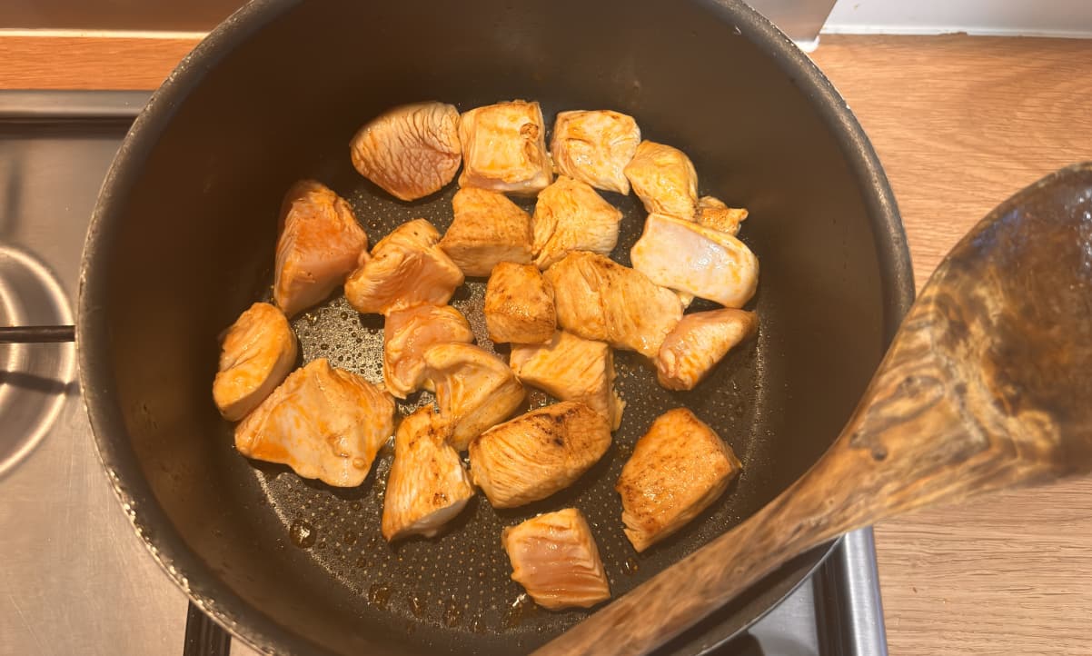 large chunks of chicken breast frying in oil and spices in a black cooking pot