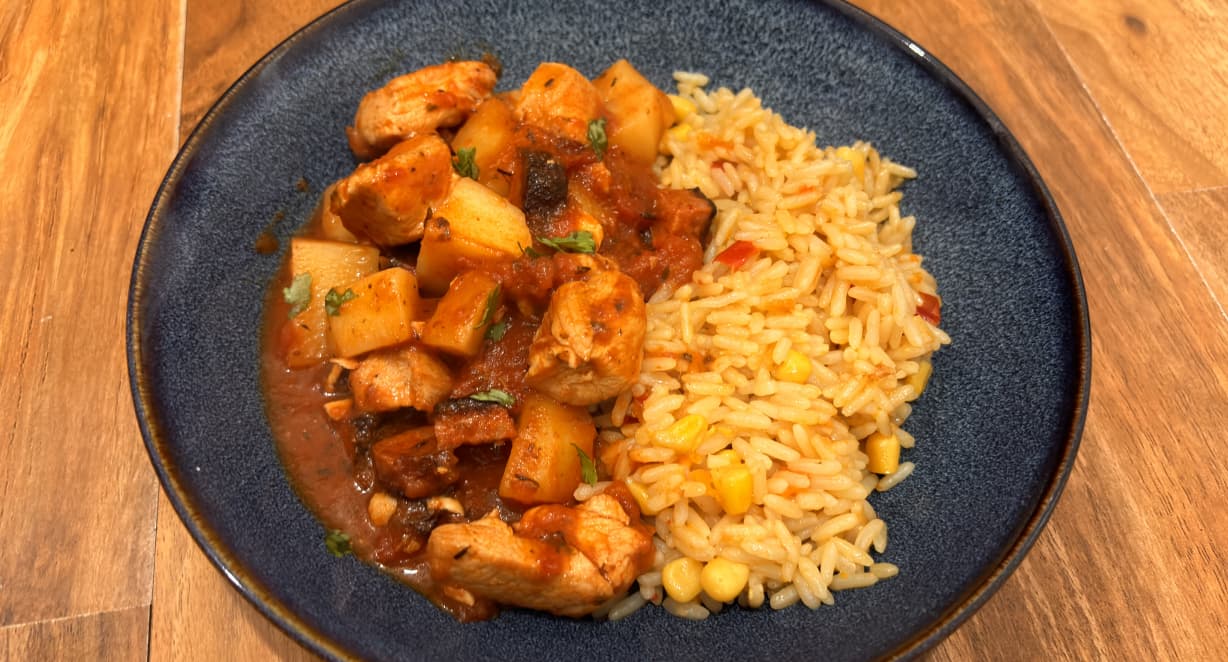 red chicken and potato stew served with savoury rice in a blue bowl