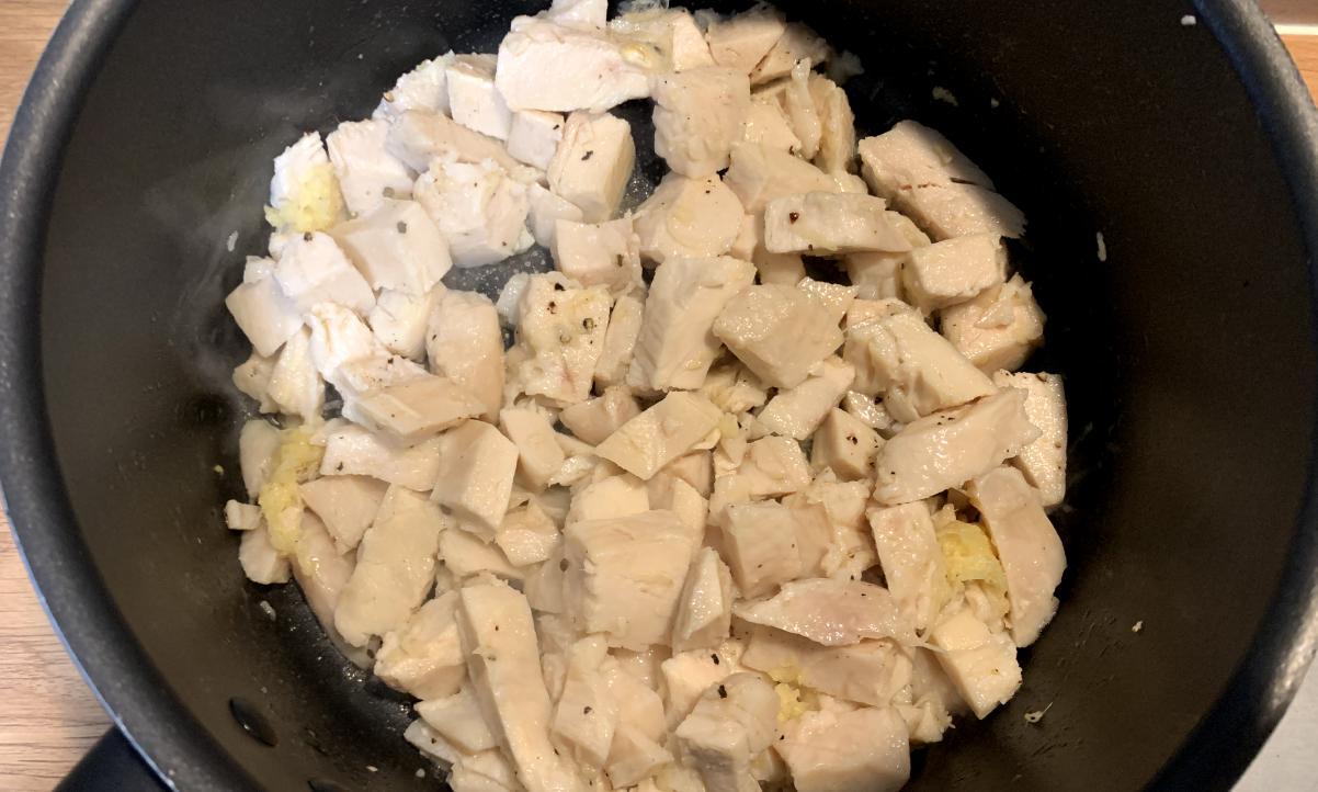 cooked chicken frying with mashed garlic and ginger in a black pot