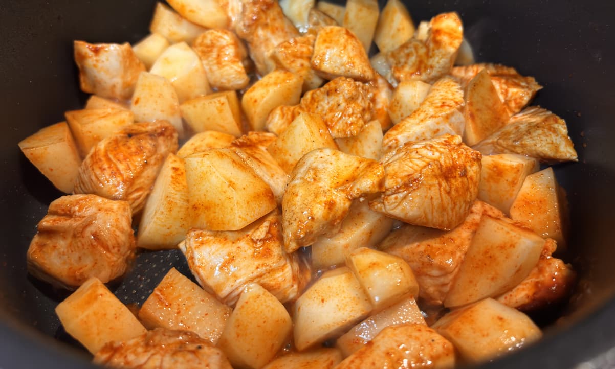 chicken and potato chunks coated with oil and paprika in a black pan