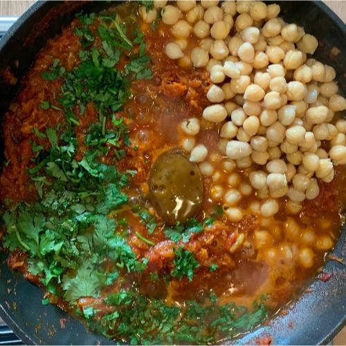 a tomato-based curry sauce in a pan, to which chickpeas, fresh corriander and a stock pot have just been added