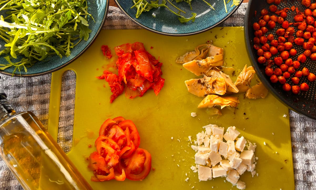 a selection of chopped salad ingredients, including kimchi and artichokes, arranged on a green chopping board