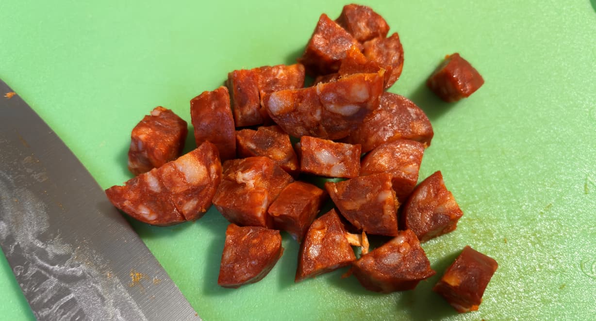 chorizo chunks on a green chopping board with a large knife in the foreground