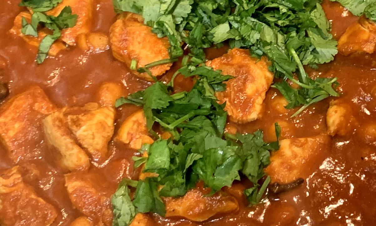 closeup of a chicken curry with a red sauce, garnished with fresh coriander