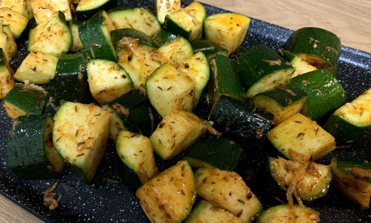 raw courgette coated with oil and herbs on a baking tray