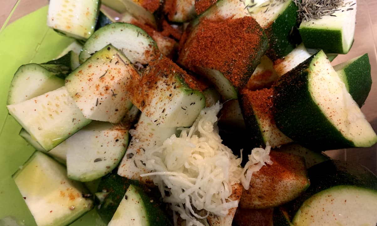 raw courgette chunks in a bowl, seasoned with powdered spices, thyme and garlic