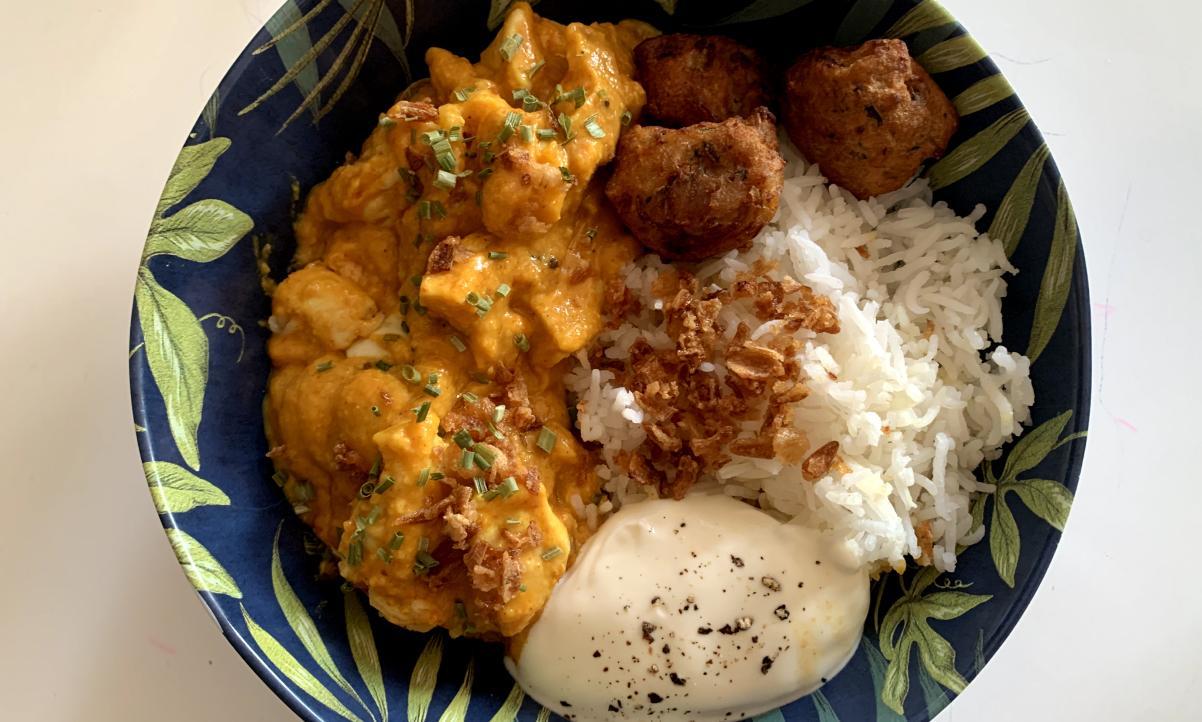 orange coloured chicken curry served with pakora and rice, garnished with chives and crispy onion