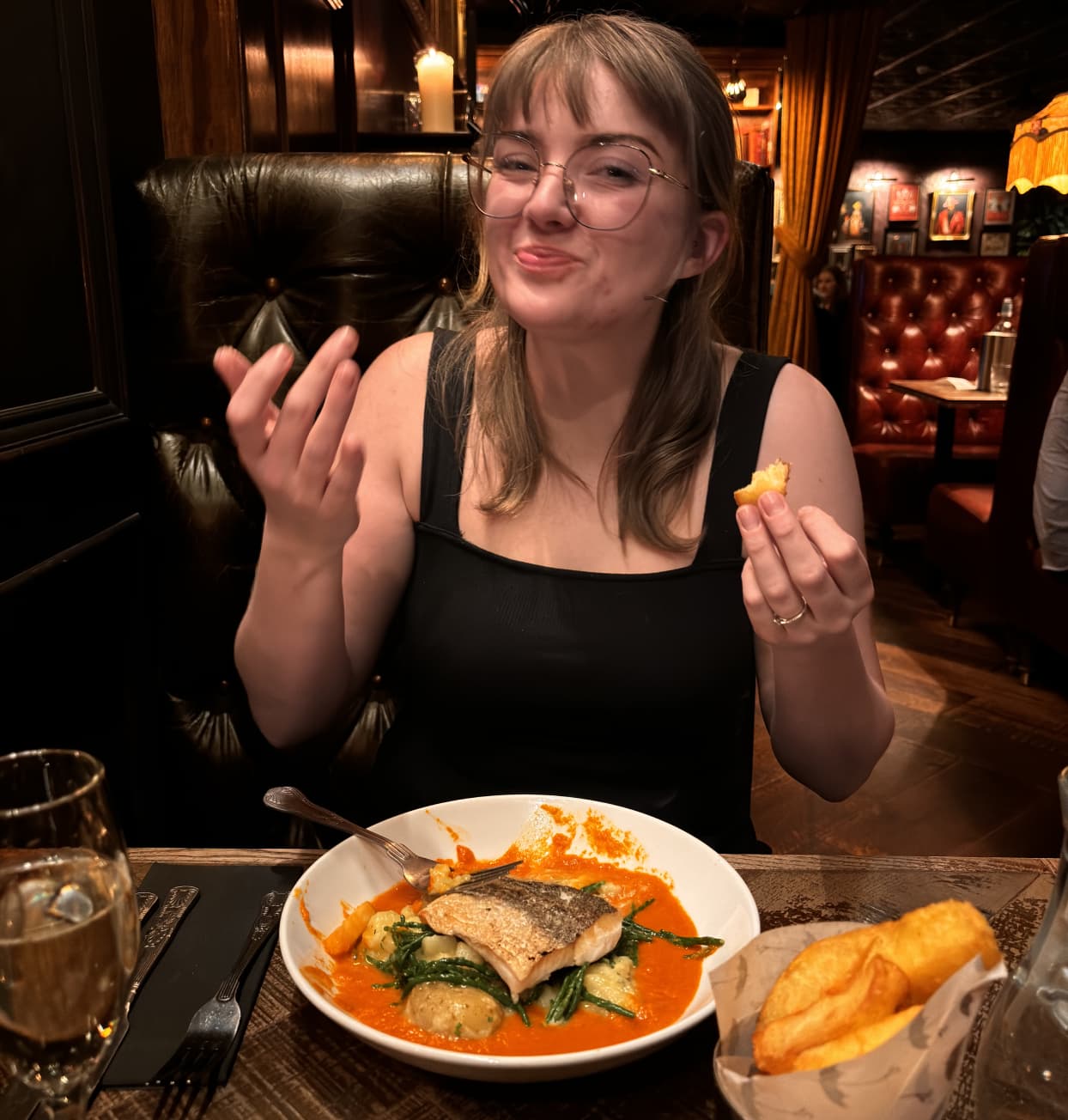 a young woman with blonde hair eating in a dimly lit restaurant, smiling