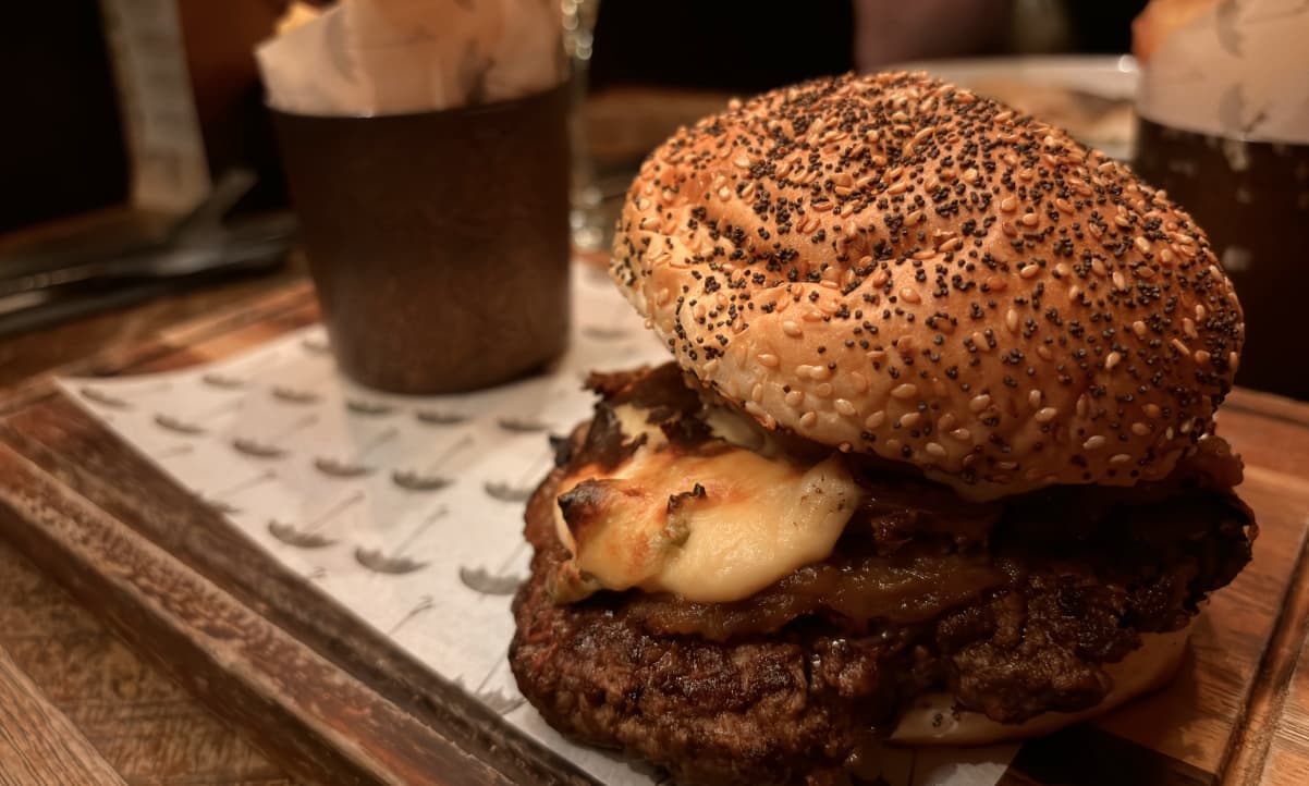 a closeup of a beef burger garnished with cream sauce, served in a heavily seeded bun