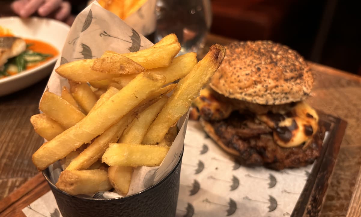 chips in the foreground, and an out of focus burger in the background on a wooden table