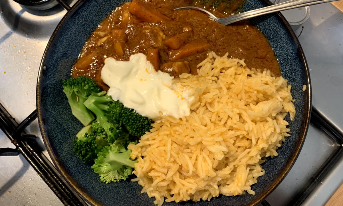 microwave rice, with a yellow hue, arranged on a blue plate with curry and broccoli