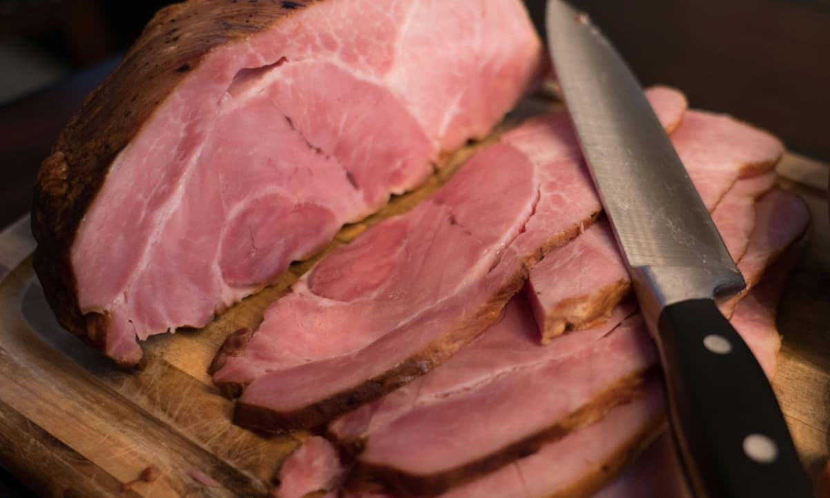 sliced pink ham on a chopping board with a large knife