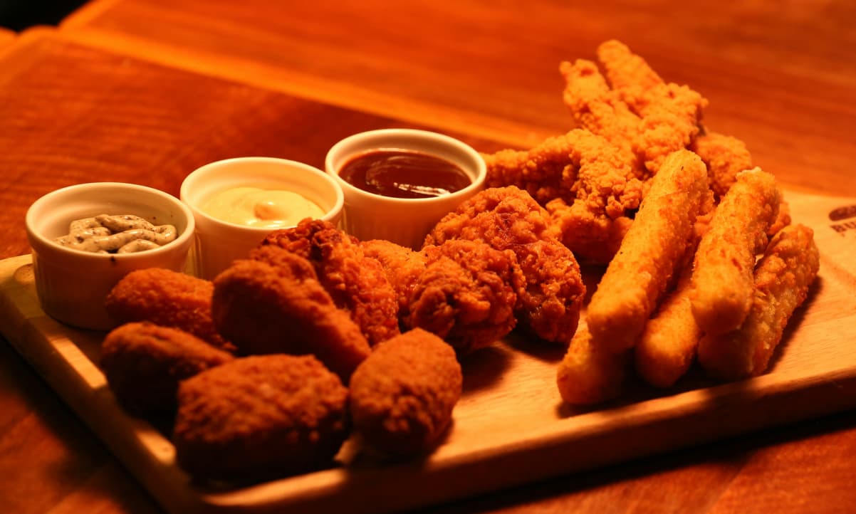 a selection of orange snacks, on a chopping board with two dipping sauces on the side