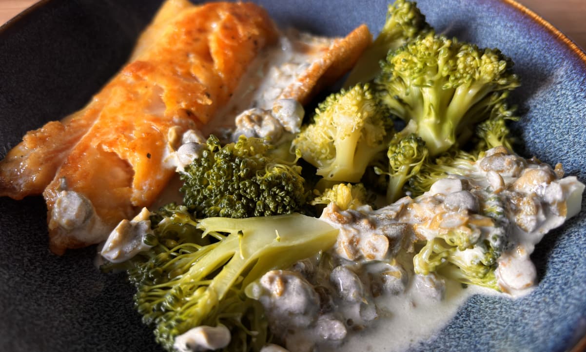 orange coloured fish fillet, with boiled broccoli and caper sauce on a blue plate