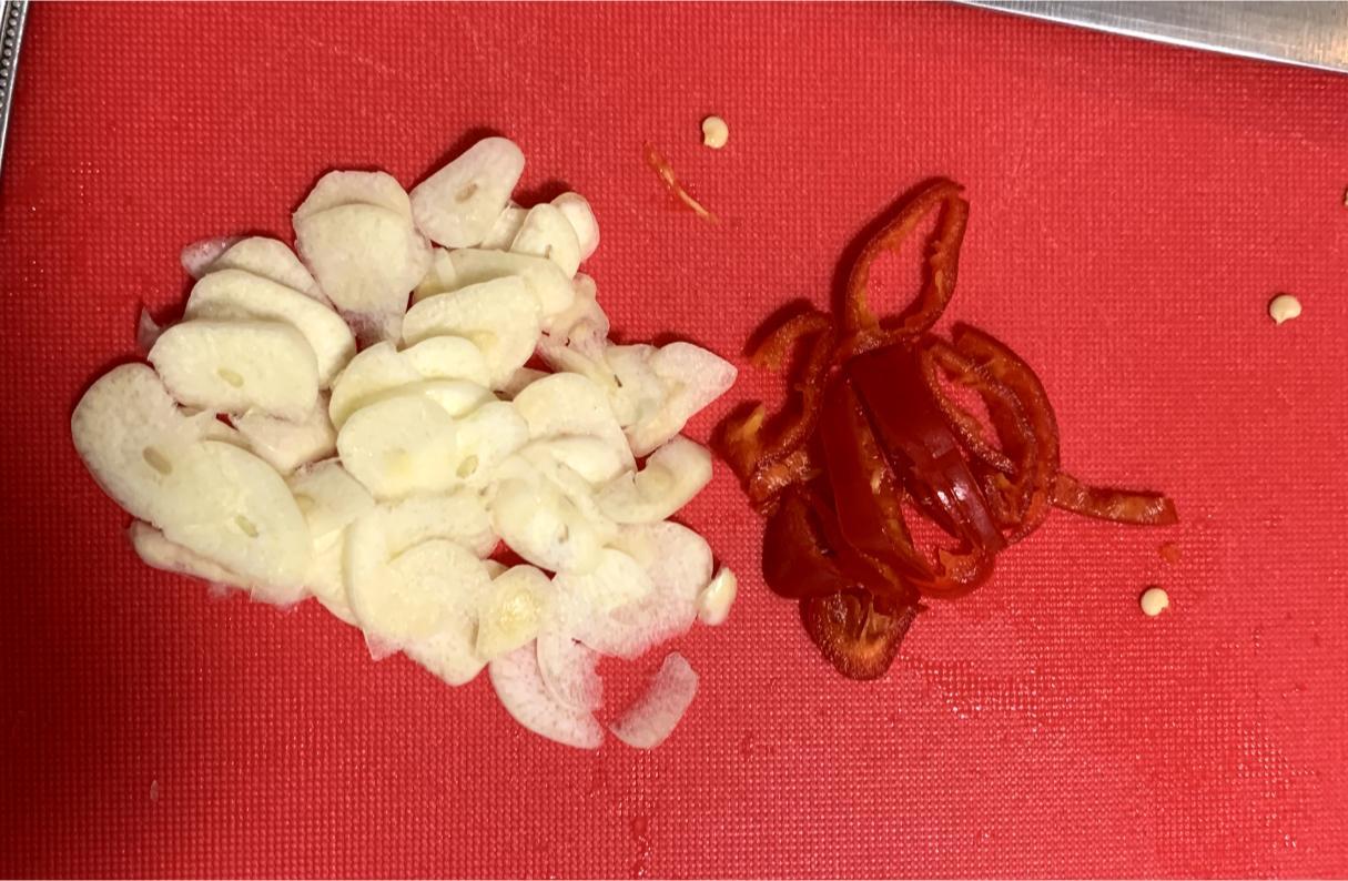 thinly sliced garlic and chilli on a red chopping board