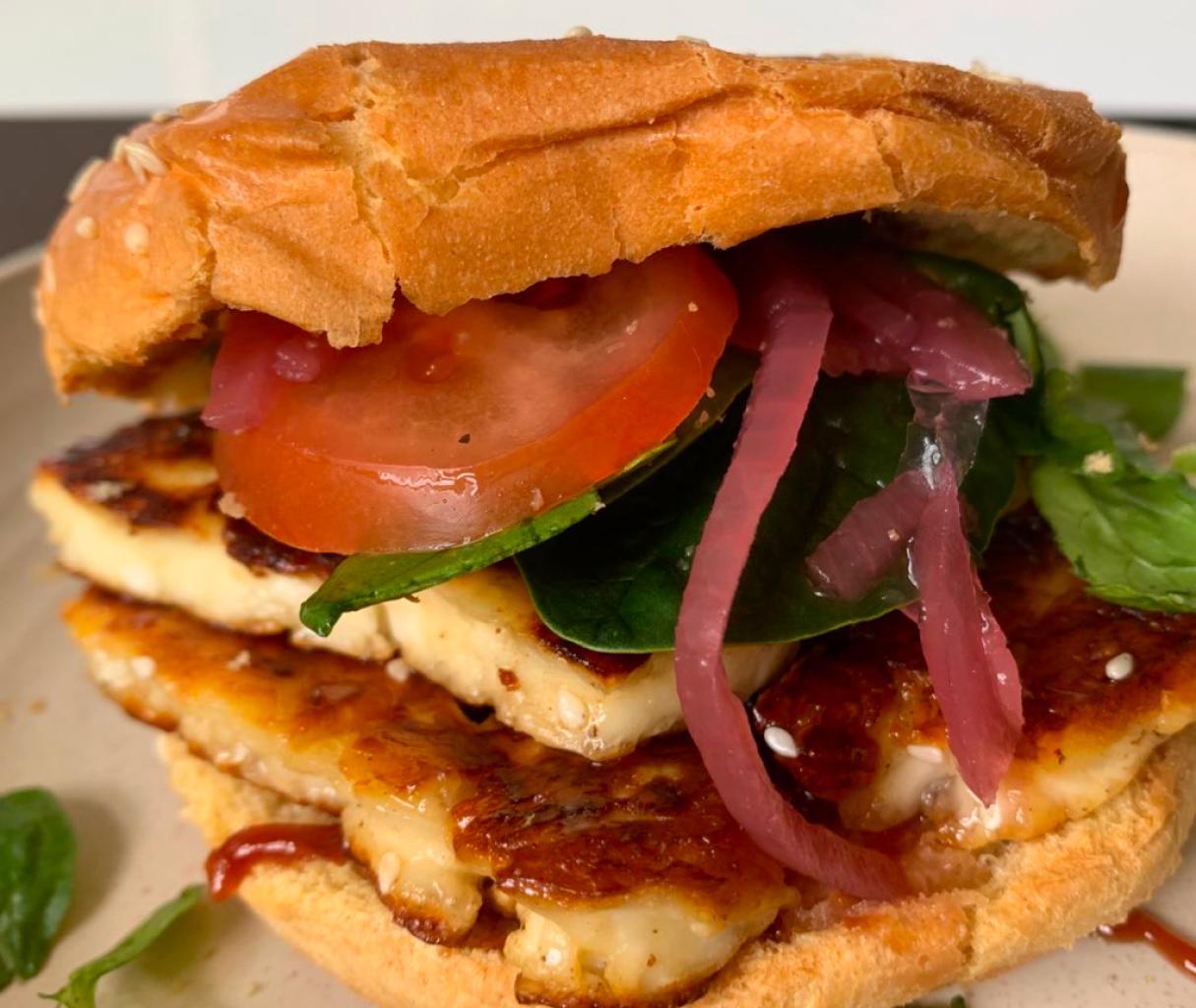 a halloumi burger garnished with salad leaves, pink onions and a slice of tomato