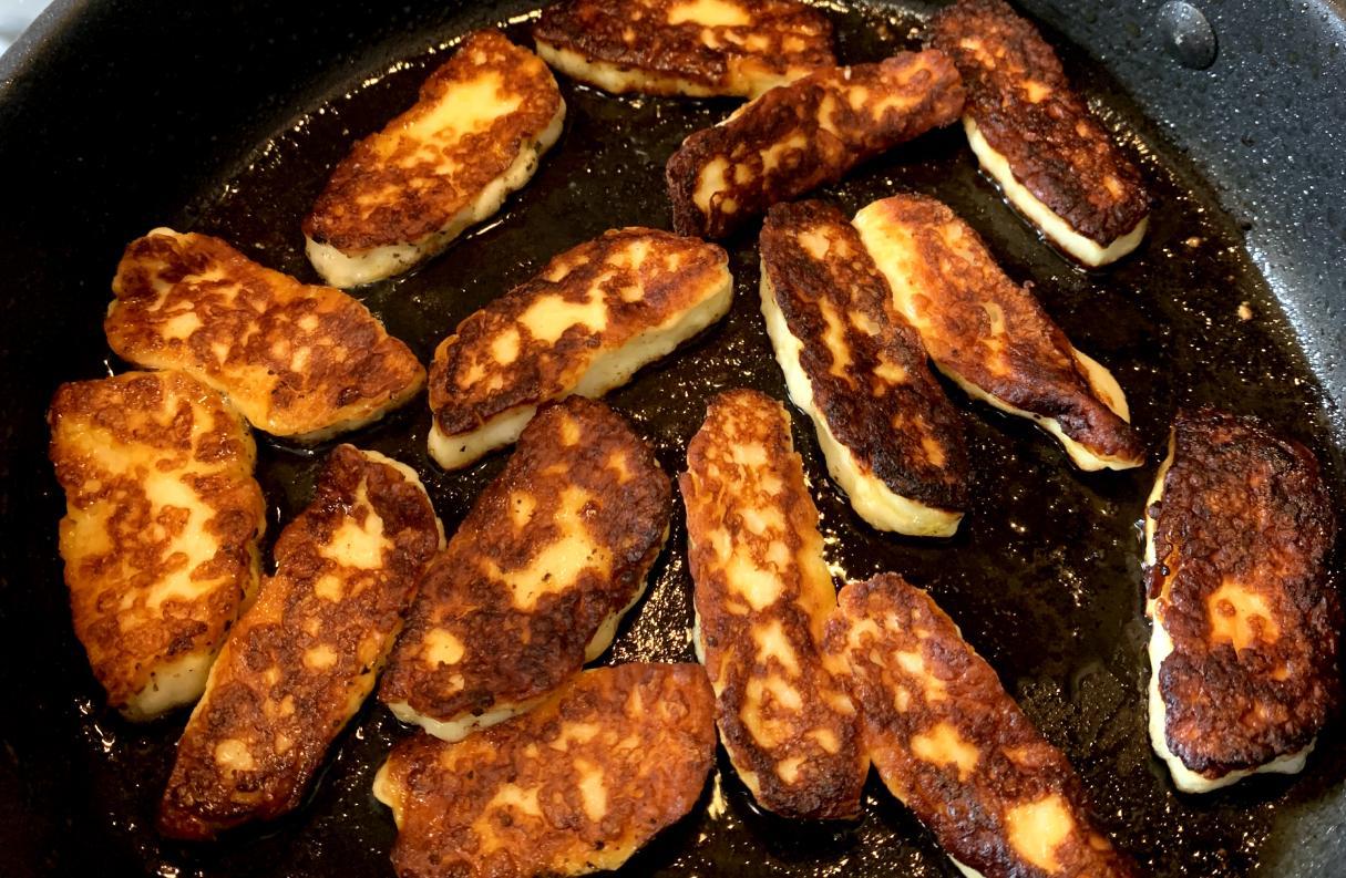 halloumi slices frying in a pan. some are slightly overcooked