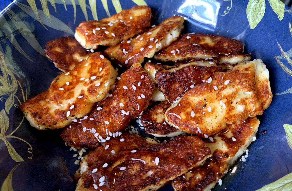 fried light halloumi slices garnished with honey and white sesame seeds