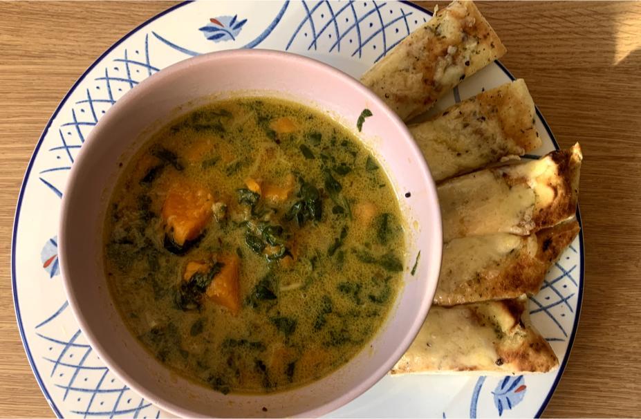 a bowl of sweet potato and coconut soup arranged on an ornate blue and white plate with slices of cheese naan