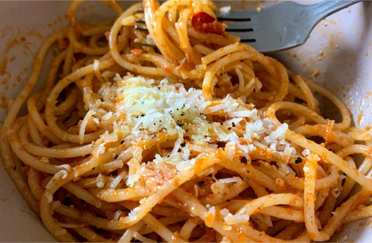 pasta and red pesto garnished with grated parmigiano, garlic and sliced chillies