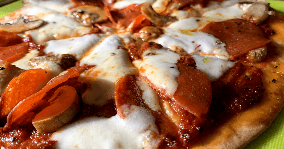 a closeup of a homemade pizza with tomato purée pizza sauce, mozzarella, pepperoni and mushrooms