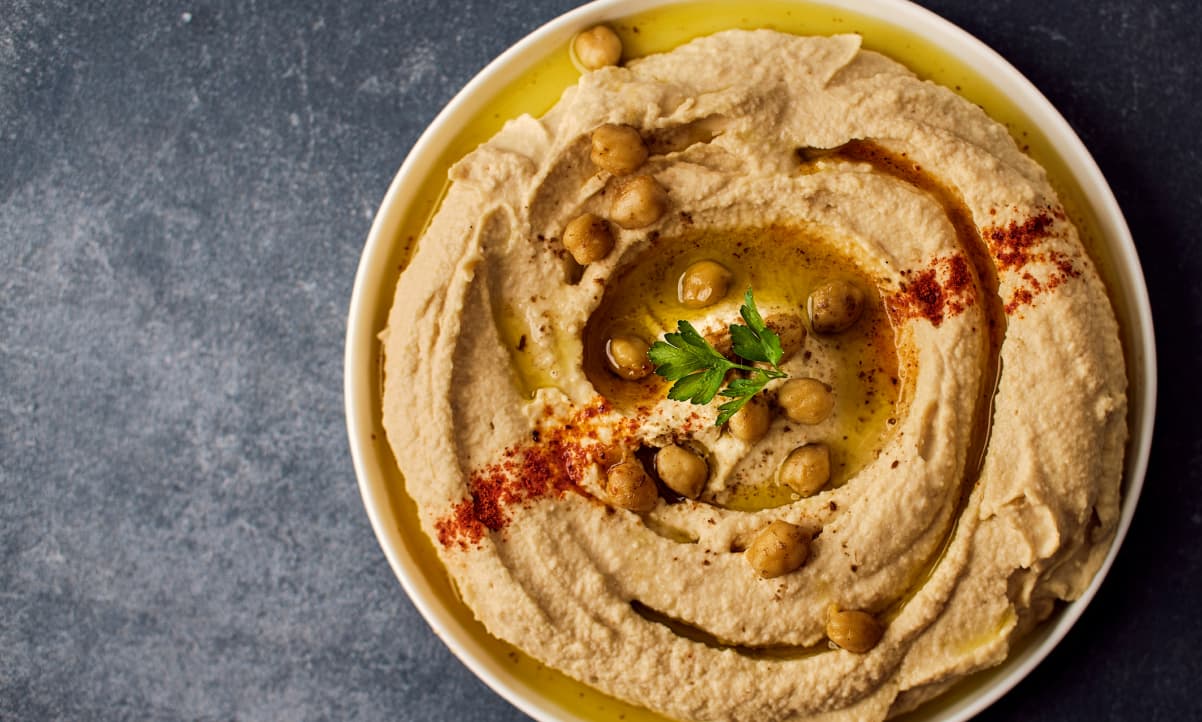 a bowl of hummus garnished with olive oil, red powdered spice and chickpeas