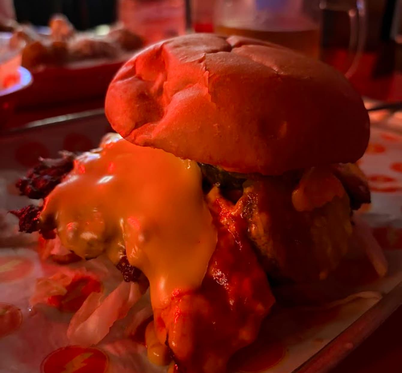 a cheeseburger on greaseproof paper with a large amount of melted cheese coming from one side and crispy bacon sticking out