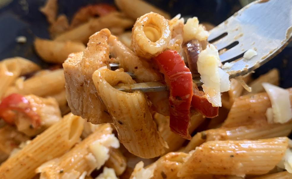 a closeup of a forkful of penne pasta coated in an orange, spicy, cream-based sauce containing chicken pieces and peppers