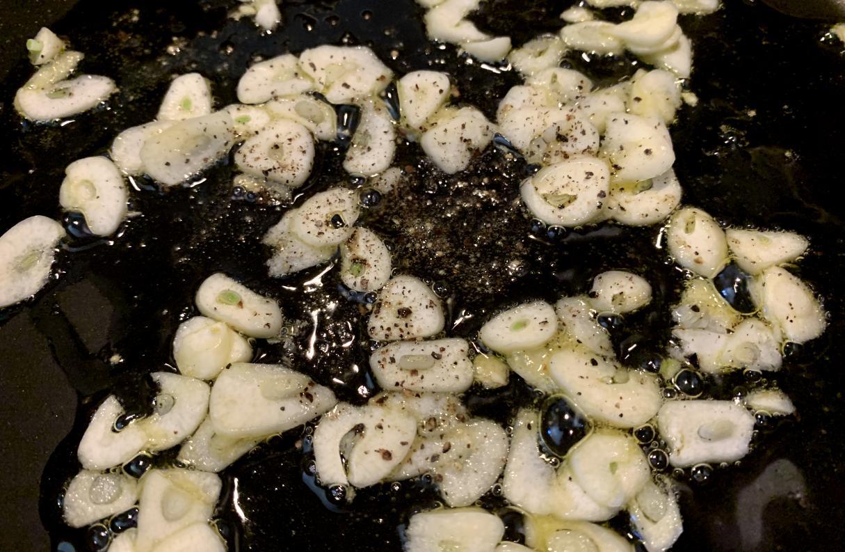 thinly sliced garlic and black pepper frying in a pan