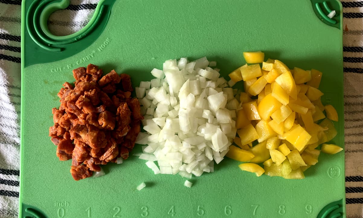 diced onion, chorizo and yellow pepper on a green chopping board