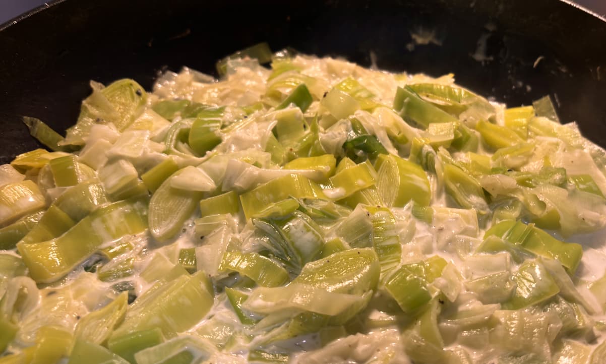 leeks in a cream sauce cooking in a black pan