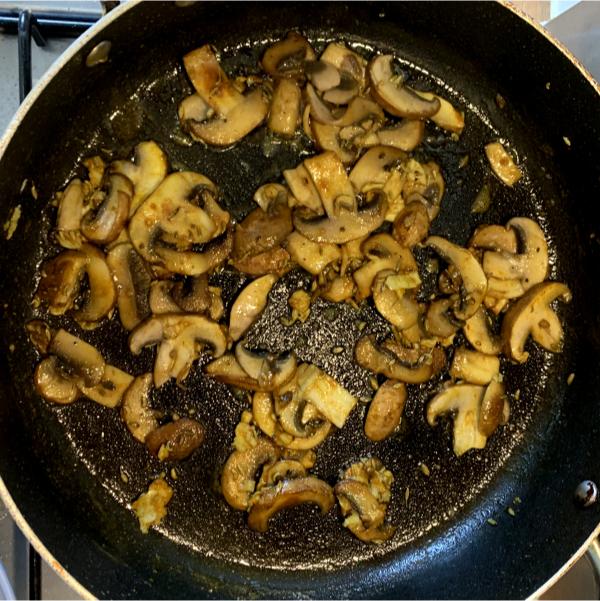 sliced mushrooms frying in a pan with spices