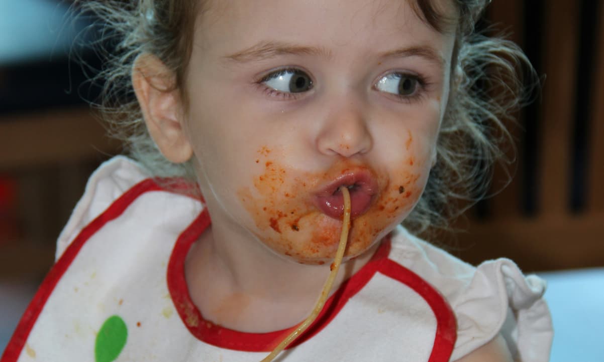 a baby eating spaghetti with sauce on her cheeks