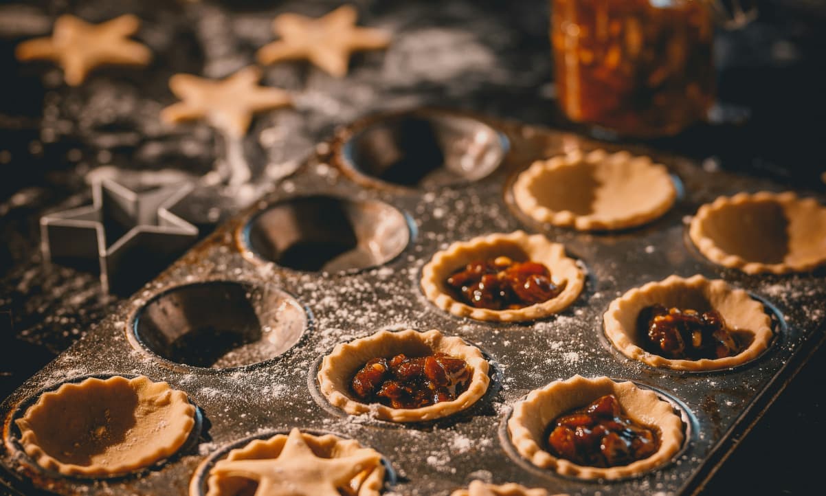 mince pie casings, uncooked, being filled on a baking tray