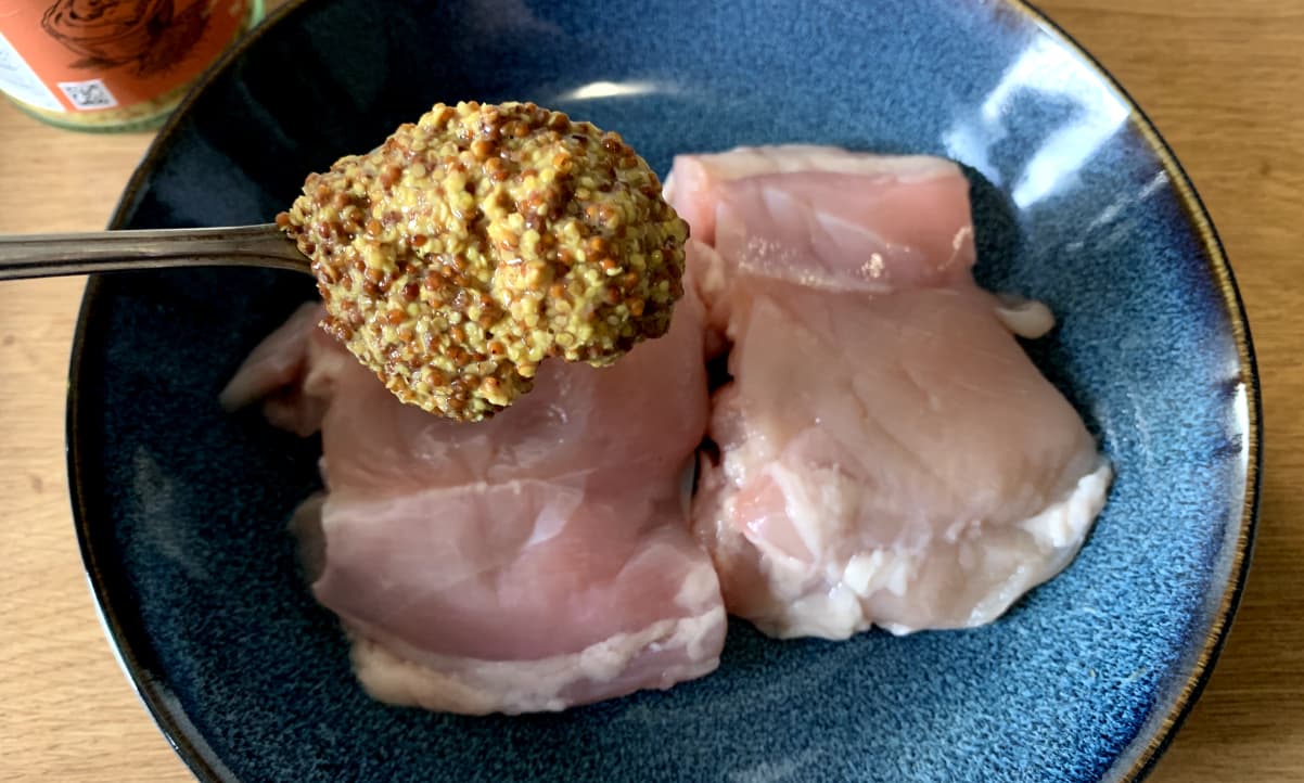 a heaped tablespoon of wholegrain mustard over a plate holding two raw chicken thighs