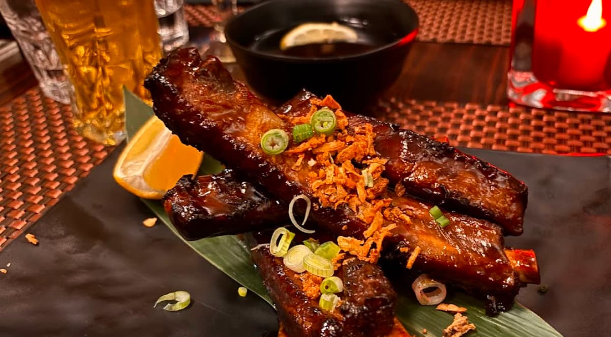 shiny and sticky pork ribs served on a black plate and garnished with crispy onions and shallots