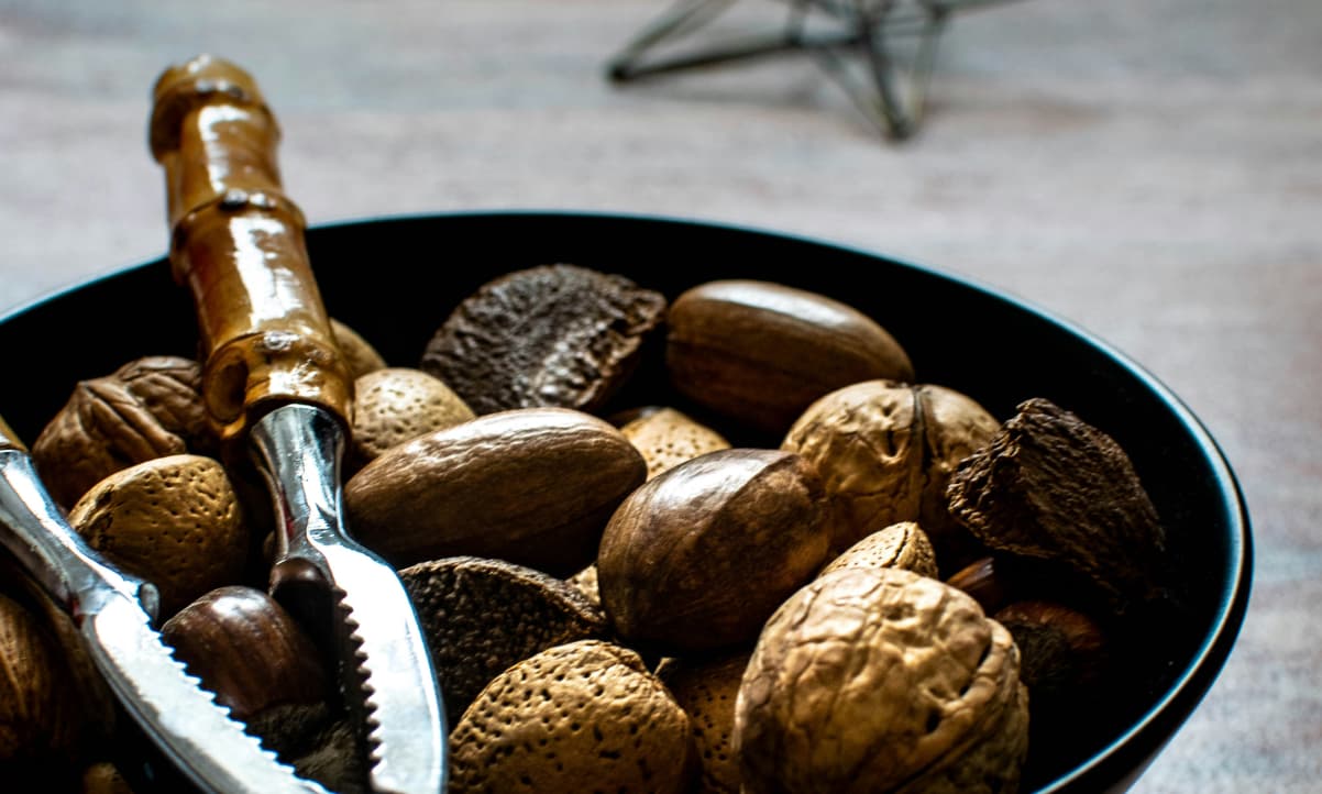 a black bowl of uncracked festive nuts like walnuts, and a nutcracker