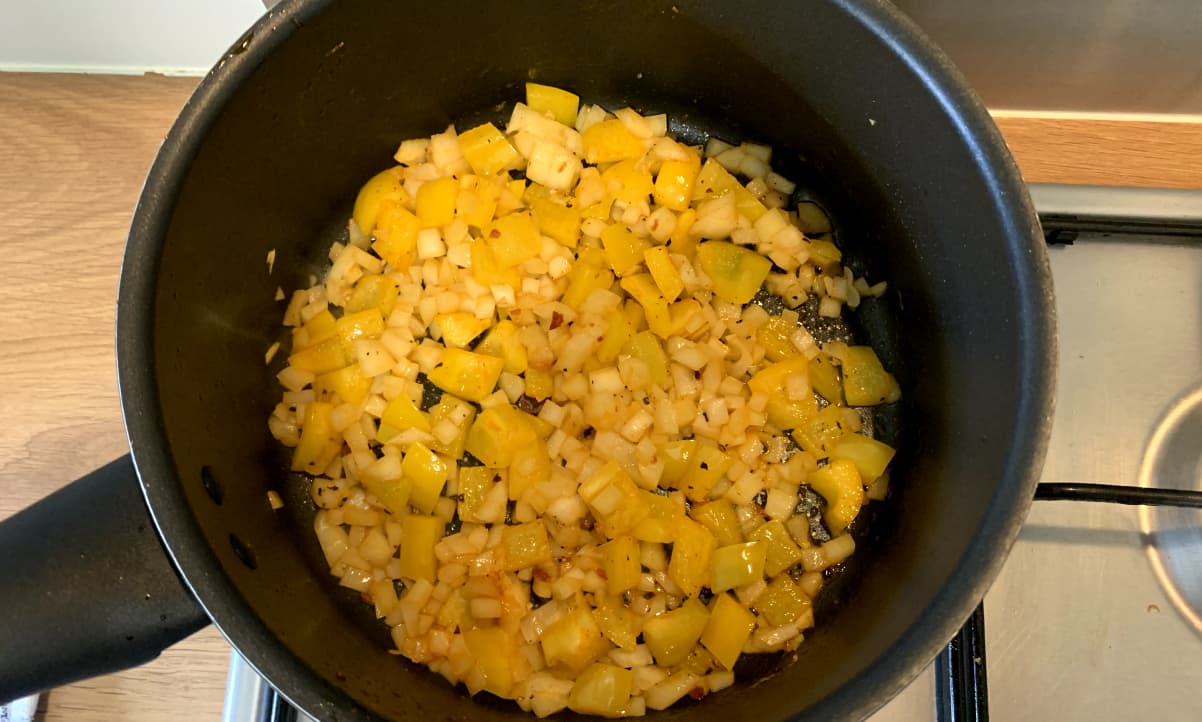 diced yellow pepper and white onion frying in a pen