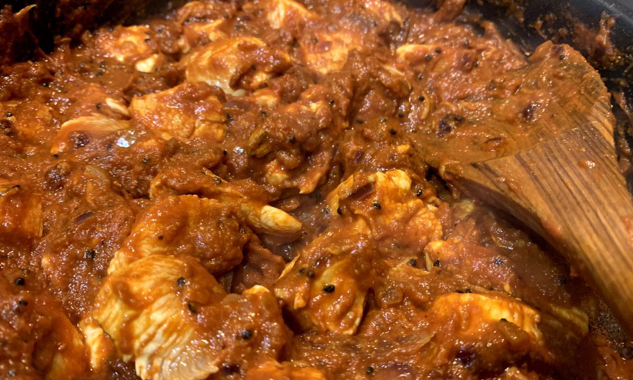 a closeup of chicken curry in a thick sauce, speckled with onion seeds